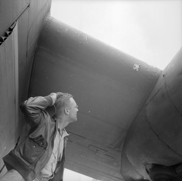 Bob Eunson, a war correspondent for Associated Press, gazes up at damage to a warplane at Wards Drome (5 Mile), an airfield near Port Moresby, New Guinea (present day Papua New Guinea). Robert Doyle notes that this photograph was taken by Sergeant Dick Hanley of <i>YANK</i>, the Army Weekly magazine, with Doyle's camera.