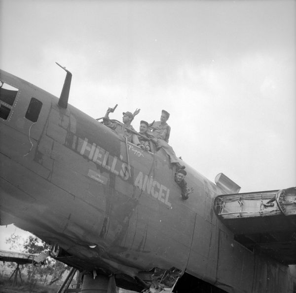 Four war correspondents, (left to right), Robert Doyle of the <i>Milwaukee Journal</i>, an unknown man, Ralph Boyce of <i>YANK</i> Army Weekly magazine and Bob Eunson of Associated Press joke around in a damaged warplane, named the "Hell's Angel," at Wards Drome (5 Mile), an airfield near Port Moresby, New Guinea (present day Papua New Guinea). Doyle and Boyce are holding weapons. The name "Pappy" is painted below the cockpit window. Robert Doyle notes that this photograph was taken by Sergeant Dick Hanley of <i>YANK</i>, the Army Weekly magazine, with Doyle's camera.