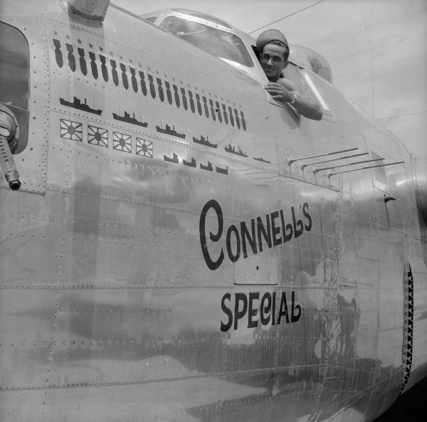 Crew Chief Master Sergeant Harold Kuba of Appleton, Wisconsin, leans out of the cockpit window of his warplane. The nose art, "Connell's Special" appears on the fuselage below him. On the left, "kill markings" appear, 23 bombs indicating 23 missions, and below, four cargo ships, one destroyer and one submarine sunk, four Zeros (Japanese warplanes) shot down and four ships damaged. The airfield is located near Port Moresby, New Guinea (present day Papua New Guinea).