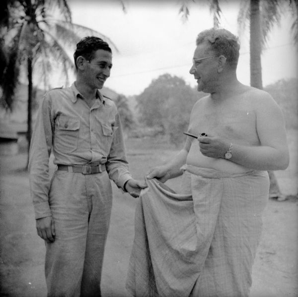 Lieutenant Richard Prentis of Detroit, Michigan, chats with Dixon Brown about his lava-lava, an indigenous kilt-like garment. Brown is smoking a pipe. Brown was a war correspondent for the <i>London News Chronicle</i>.