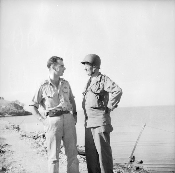 War Correspondent Robert Doyle and Lieutenant Colonel Philip F. La Follette, wearing combat uniform, chat while standing on a shoreline. Lieutenant Colonel La Follette was three times Governor of Wisconsin. He took part in the landings at Cape Gloucester, New Britain Island, in charge of a group of press correspondents.