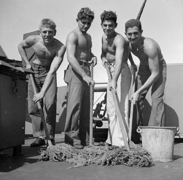 Mopping up after the bombardment of Cape Gloucester while the American cruiser returns to base are: (left to right, all shirtless) Seaman 2nd Class Dominick Gresinanno of Brooklyn, New York, Seaman 2nd Class Pandillis Perris of Bronx, New York, Seaman 1st Class Edward Presutti of Staten Island, New York and Seaman 2nd Class Daniel Koepp or Milwaukee, Wisconsin. Cape Gloucester was located in New Britain, New Guinea (present day Papua New Guinea).