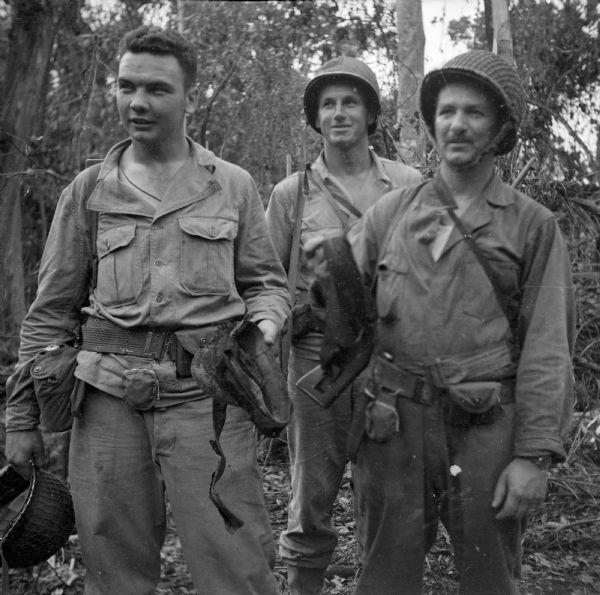 Robert Doyle's caption reads, "Wisconsin artillerymen hold Japanese caps they found a few minutes after landing at Saidor, New Guinea. Left to right are Warrant Officer Carl Wilke of Mauston, First Lieutenant Richard A. Kinzer of Milwaukee and Captain Riley B. Robinson of Mauston." The jungle is in the background.