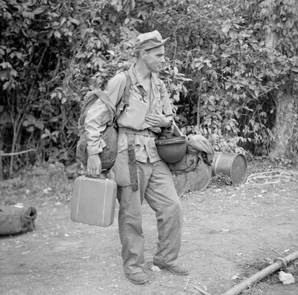 War correspondent Murlin Spencer of Associated Press is loaded down with his gear as he prepares to leave Dreger Harbor for Cape Gloucester, New Guinea (present day Papua New Guinea). The jungle is in the background.