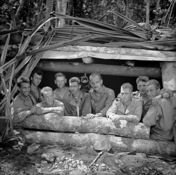 Artillerymen of Battalion A are ready for an enemy attack in a gun pit, at Saidor, New Guinea (present day Papua New Guinea). A knife is standing point down in the front log. Names (left to right) are Sergeant Robert Ledin of Milwaukee, Wisconsin, Private First Class Charles Evans of Hutchinson, Kansas, Private Charles Mahoney of New York City, Private First Class William Rentfro of Effingham, Illinois, Corporal Frank Parr, Lieutenant Robert Winkenwerder, Private Lawrence Barth, Private Frank Parys and Private Gordon Fabry, all of Milwaukee, Wisconsin.