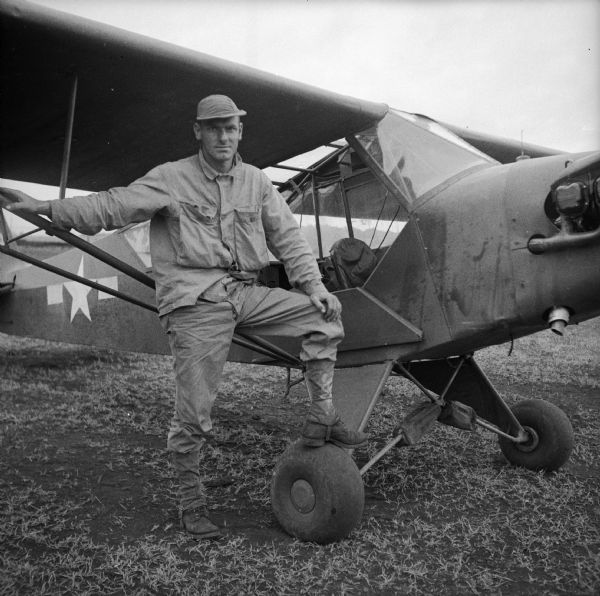 Pilot Staff Sergeant James P. Baldwin of Houston, Texas, poses standing with his Piper Cub at the Saidor Airstrip, New Guinea (present day Papua New Guinea).