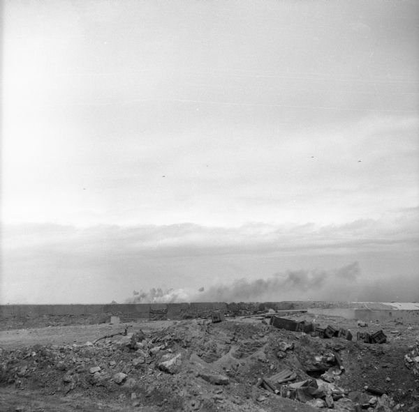 Smoke rising from Cezembre Island, just north of Saint-Malo on the north coast of France. The island, which took a tremendous shelling, can barely be seen over the embankment. It was German-occupied until the Allies mounted an operation to seize the island starting August 21st. The Allies made five trips under a white truce flag before the Germans obtained permission to surrender. They surrendered on Saturday evening, September 2nd. Saint-Malo and Dinard were recently liberated from the Germans on August 15th and the citadel in the harbor fell three days later. That may be the source of the rubble and broken material seen in the foreground.