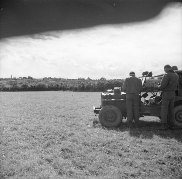 View of distant smoke from the battle surrounding Brest, France. In the foreground, soldiers are parked in a large field with an air support radio jeep. They are controlling Allied dive bomber numbers. A belt of trees appear between the field and the distant town. Eventually, after a fierce defense, the Germans surrendered Brest to the Allies on September 18th.