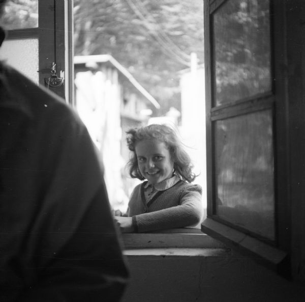 View from indoors of a smiling eleven-year-old girl posing in an open window that opens onto the street in Landerneau, France. Robert Doyle, war correspondent for the <i>Milwaukee Journal</i>, notes that she has freckles.