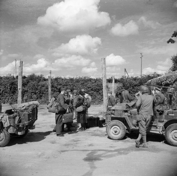 High-ranking German Naval Officers arriving at the prisoner of war cage at the 2nd Division Camp at Guipavas, France. Allied soldiers are standing guard and jeeps are parked on the right and left. Behind the jeep on the right is a 105mm Howitzer under camouflage netting.