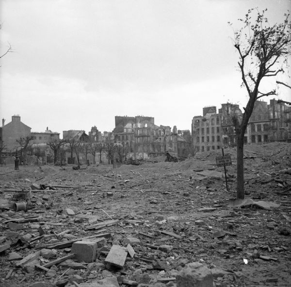 Rubble and destruction in Brest, France. A few trees and a sign are still standing. Bombed-out buildings are in the background. Robert Doyle's caption reads, "Desolation and destruction mark President Wilson square in Brest, France, on afternoon of surrender of city."