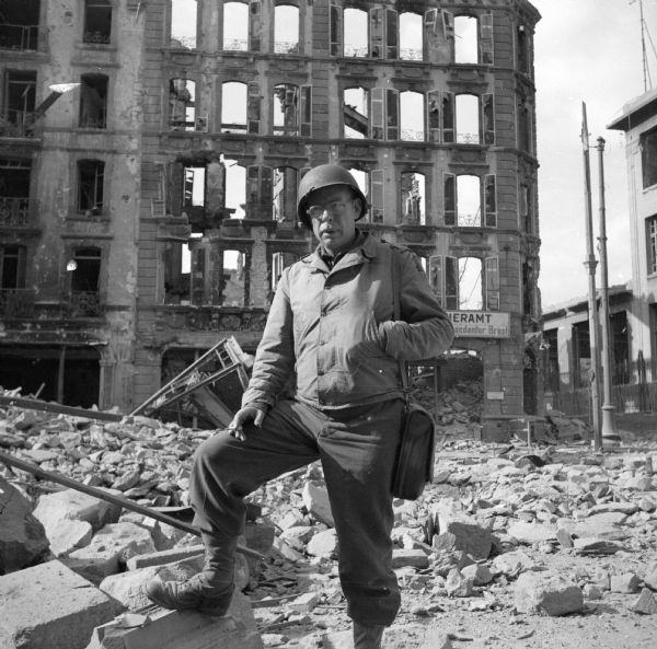 Allied soldier posing in Brest, France, in front of a bombed-out building, smoking a cigarette. The street is covered with rubble.