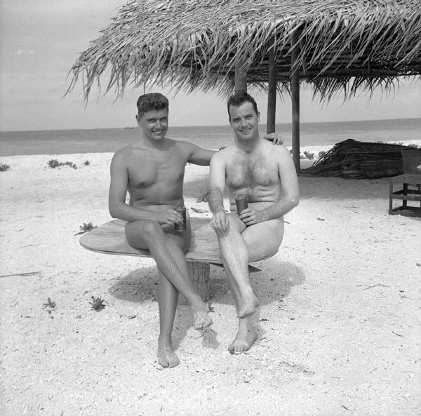 The caption in the <i>Milwaukee Journal</i>, says it best, "From the far-off Pacific (somewhere on Kwajalein), the picture of Ensign Ray Hanson and Robert Doyle came to <i>The Little Journal</i>. What a contrast in sun tans it provides! Ensign Hanson, formerly of the editorial department of <i>The Journal</i>, is an administrative officer in the Naval Air Transport Service (NATS), and Doyle, <i>The Journal's</i> accredited war correspondent, is doing pieces on Wisconsin boys anywhere he finds them on his long sojourns." What the paper did not reveal, was that both men were having a nude sun bath, this was not apparent because the paper had added black swim trunks to the photo. Both men are holding a metal beverage bottle. A thatched beach shelter and the Pacific Ocean are behind them. The Kwajalein Atoll is in the Marshall Islands, in the South Pacific.