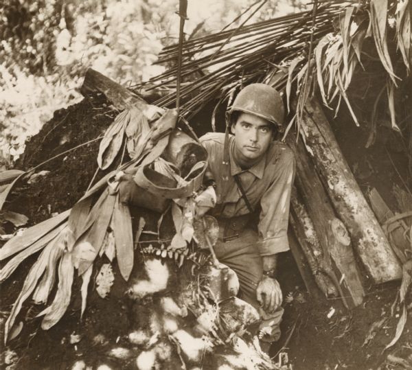 Robert Doyle emerges from a captured Japanese pillbox at Buna, New Guinea, (present day Papua New Guinea). The pillbox is built of dirt, logs and foliage.