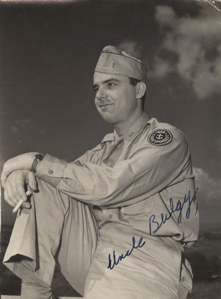 An outdoor casual three-quarter length portrait of Robert Doyle in his war correspondent's uniform. He is holding a cigarette. Sky, clouds and countryside are in the background. Handwritten across the lower right corner is "Uncle Bulgy."