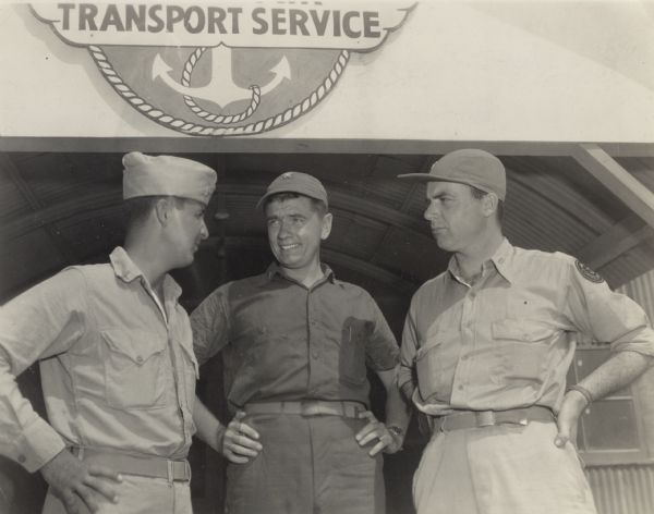 From the caption that accompanied the image: "Fellow workers in civilian life, these Milwaukeeans met recently on Kwajalein atoll in the Marshall islands. The are (from left) Lieutenant Louis Olszyk, on leave from The Journal news staff, now officer in charge of the 4th marine air wing news service at Kwajalein; Ensign Ray Hansen, also on leave from The Journal news staff, who works in the naval air transport service office at Kwajalein and Robert J. Doyle, The Journal's staff war correspondent. They are chatting beneath the "Naval Air Transport Service" sign on a building at the airfield.