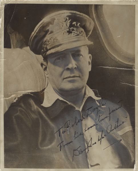 An autographed quarter-length portrait of General of the Army Douglas MacArthur seated on an airplane near a window. He is wearing his uniform with a jacket and hat. Handwritten across the lower right corner is "To Robert Doyle, From his home town friend, Douglas MacArthur." On 18 April 1942, MacArthur was appointed Supreme Commander of Allied Forces in the Southwest Pacific Area (SWPA). He was promoted to General of the Army shortly before the end of 1944. In a letter, dated March, 14th, 1945, MacArthur awarded Robert Doyle the "Asiatic-Pacific Service Ribbon in view of your long and meritorious service in the Southwest Pacific Area with the forces of this command. You have added luster to the difficult, dangerous and arduous profession of War Correspondent."
