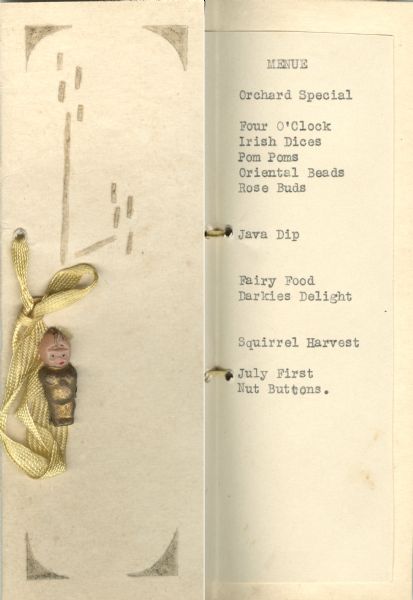 Handmade menu decorated with gold ink and bound with a golden ribbon, accented with a pinned-on baby doll with a gilded body.
