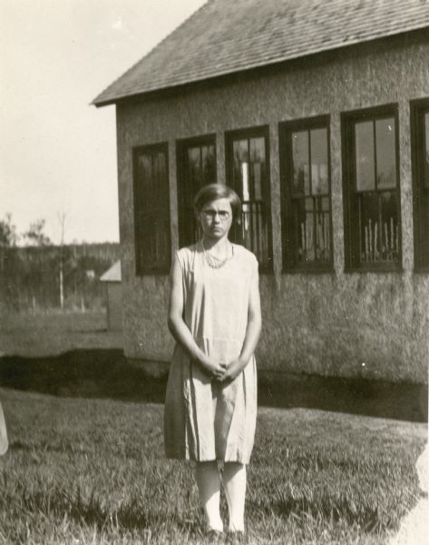 A girl posing at the side of the Miles District No. 2 School. Selected as the "girl 4-H champion," Emilie, age 12, was noted by her teacher as "an outstanding personality" and that "she won a free trip to Madison in connection with 4-H work."