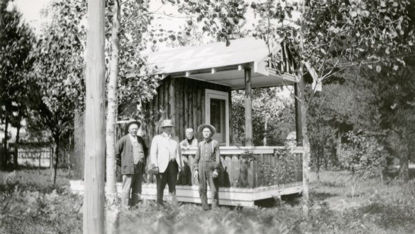Three men and a boy pose in front of a small rustic cottage. They are, from left to right: Alb. Hernke, Hilbert; George Duchow and his son Armin, Potter; and Louis Burkhardt, Sheboygan. The cottage belonged to Mr. Burkhardt. The photograph was submitted to the Wisconsin Rural Schools Survey as an example of "Where Pupils Travel." Armin Duchow was a student at the Potter School, District No. 3, Town of Rantoul.