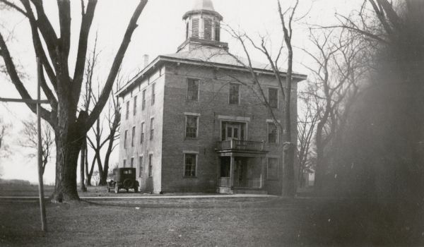 North Hall, also known as Chapel Hall, on the campus of Albion Academy. The three-story structure is of brick and has a large cupola. A car is parked alongside the building. The Academy, established by Seventh Day Baptists in 1853, closed in 1918. North Hall was owned by the Town of Albion at the time of this photograph.