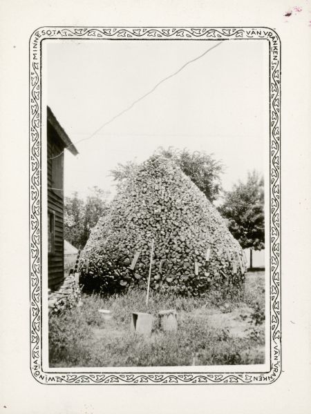 A conical stack of stovewood owned by Delbert Karns of 9th Street, Menomonie stands beside a house. It contained 55 cords of wood.
