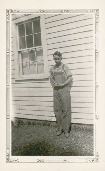 Ivan Rhyner, 13, "leader of highest class in history" at Farmer's Grove School, poses outside the school holding a book.
