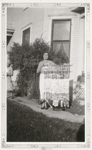 Elda Strahm, 13, poses outside her home with many prize ribbons which she won at the Green County and Wisconsin State Fairs. Another girl stands on the left. On the reverse of the photograph is written, "A very industrious, ambitious, and energetic student."
