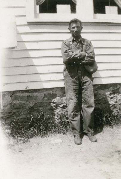 Jake Wepking, clerk of School District No. 4, poses in front of the Strawberry School. He is wearing bib overalls and holds a cap in his hand. Wepking was a respected farmer in the area.