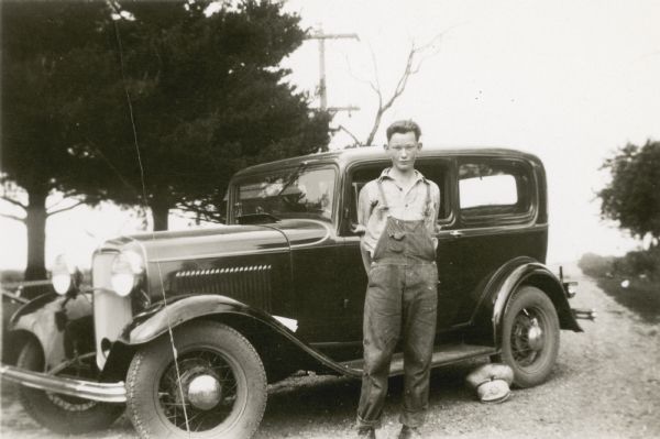 Russell Wepking, 14, posing beside an automobile. The son of Frank Wepking and a student at Strawberry School, Russell "Won distinction of having Grand Champion 4-H Club calf and also won first in Showmanship contest in 1930 Highland High School Fair." His hat is lying on the ground near the car's rear tire.