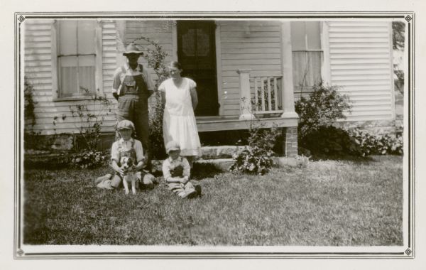 Oscar Hendrickson and his wife pose with their sons Kenneth and Myron in front of their house. Kenneth, a student at the Mud Branch School, District No. 2, holds a small dog.