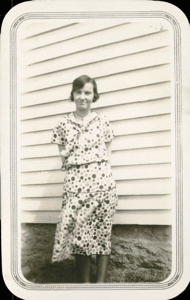 The teacher at Eagle Corners School, District No. 3, Township of Eagle, Gladys Hofseth, poses in front of the school. She is wearing a polka dot dress.