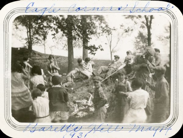 Students from the Eagle Corners School, District No. 3, Township of Eagle, roast marshmallows over a fire at Barett's Hill (spelled Barrett's on the reverse of the photograph.)