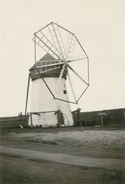 A windmill with eight vanes stands along an unpaved road. The mill was built by Jacob Davidson in 1904 to grind flour and livestock feed. Davidson hand-hewed the framing, shafts, gears and shingles for the mill.