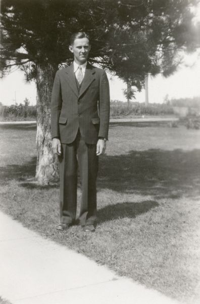 Kermit Schulz poses in front of a pine tree wearing a three piece suit. He is the teacher at Rhine Center School, District No. 6.