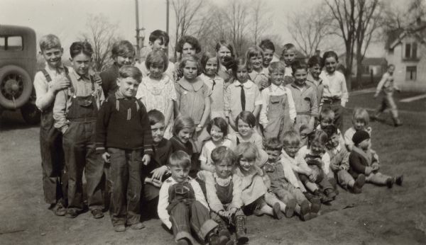 Students of the Honey Creek School, District No. 1, pose in the school yard. There is a car in the background.