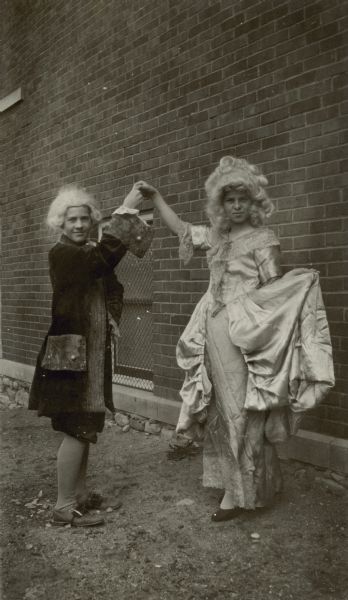 Two students at the Honey Creek School, District No. 1, pose as if dancing a minuet outside of the school building. The boy and girl are dressed in Eighteenth Century costumes, complete with wigs. They performed at the George Washington Bicentennial birthday program at Honey Creek Hall.