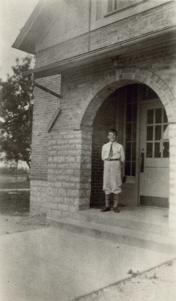 Roger Baird, 11 years old and a student at Hillcrest School, District No. 6, Towns of Waukesha, Pewaukee, Brookfield and New Berlin, poses on the arched front porch of the school building. He is wearing knickers and argyle pattern stockings. Roger was the "Leader of highest class in mathematics" as well as "The Inventor." On the reverse of the photograph is written that he "Invented a contrivance that mixes wheat with other grains evenly."