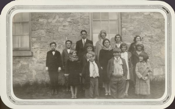 Students at Victory School, La Crosse County, pose at the side of their stone school building.  All the boys are wearing neckties.