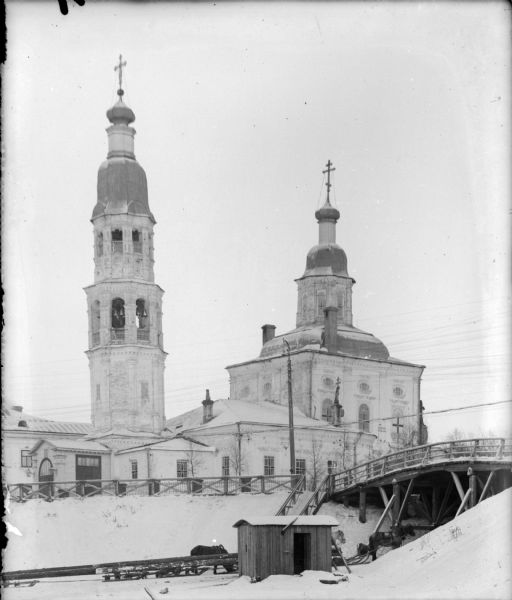 Exterior view of the Church of Uspenanski Bogoroditski. This building also served as an American hospital in Archangel [Arkhangelsk], Russia during the Allied Northern Russia Intervention. On the right horses stand in the snow underneath a wooden bridge that crosses a gulley to the hospital.