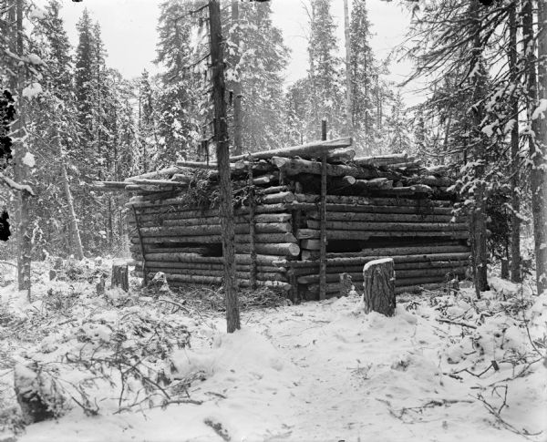 A log blockhouse under construction to support the Allied Intervention in Northern Russia. The fortification is surrounded by a forested area covered in snow.