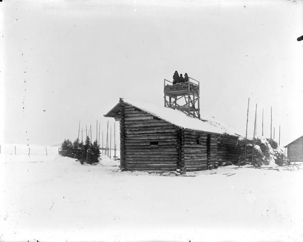 View across snow-covered ground towards a machine gun emplacement and its three man crew on the roof of a shed.