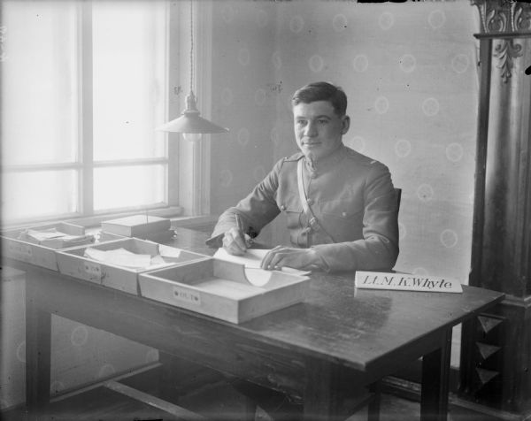 Indoor portrait of Lieutenant M.K. Whyte from Company B, of the 310th United States Engineer Corps, in uniform, sitting at his desk near a large window.