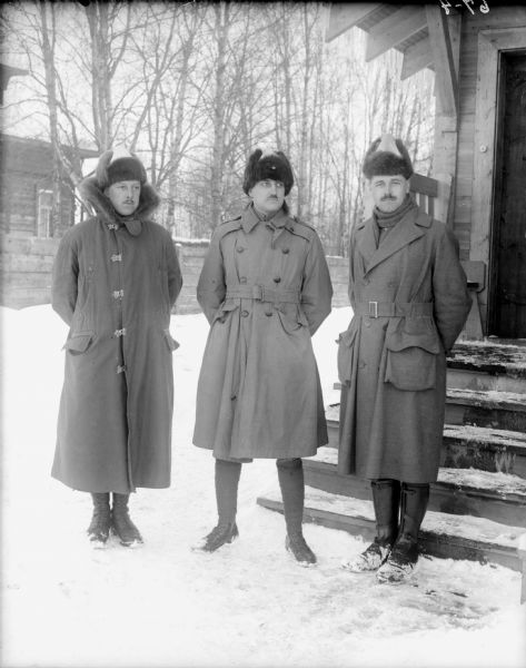 Group outdoor portrait of the officers of the 310th United States Army Engineer Corps, standing left to right: Lieutenant H. Pryale, Company C; Colonel P.S. Morris, Commanding Officer, 310th United States Army Engineer Corps; and Lieutenant. R. Jens, Company C. In the background across the snowy yard is a wooden fence and behind it another building.
