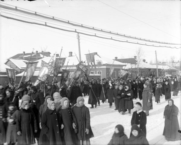 A large group of Russians conducting a religious parade through a town. The men in the group are carrying the iconography.