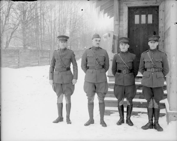 Group portrait of the staff officers of the 310th U.S. Army Engineer Corps. Lieutenant colonel P.S. Morris, the Commanding Officer, is standing second from the left. The group is posed outdoors in the snow, and behind them is a wooden building with a bench on the small porch.