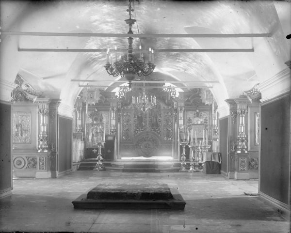 Interior of the Troitski Cathedral, showing the altar of the cathedral, chandeliers, large floor candle holders, and iconographic wall panels.