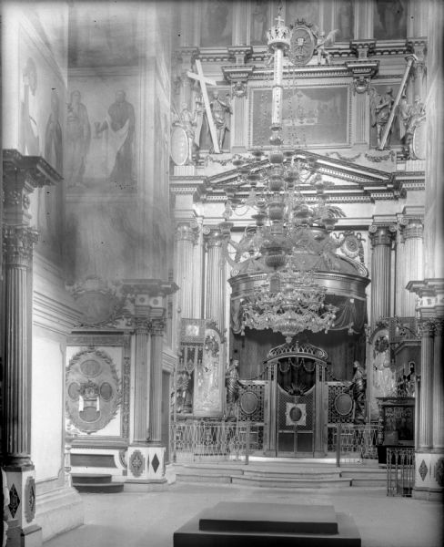 Interior of the Troitski Cathedral, showing the altar of the cathedral, chandeliers, large floor candle holders, and iconographic wall panels.