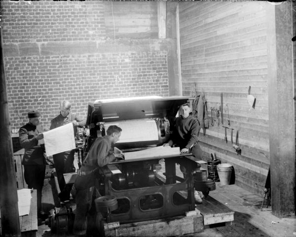 Four soldiers printing on a press. Two men are reviewing maps, and the other two men are standing at the lithographic press of 310th U.S. Army Engineer Corps.