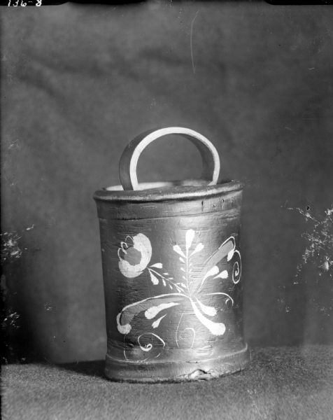 A Russian birch bark container, including a top with a handle, and a painted floral design. The container was used to carry items from the market.